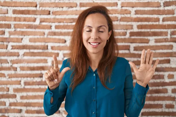 布鲁内特女人站在砖墙上 用七号手指指指着 自信而快乐地微笑着 — 图库照片