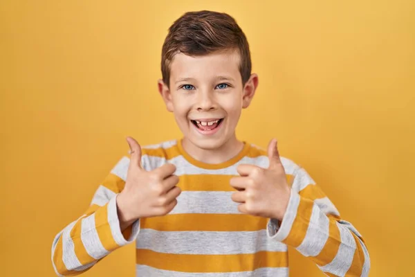 年轻的高加索小孩站在黄色背景的成功标志前 用手做着积极的手势 竖起大拇指 微笑着 快乐地 快乐的表达和胜利的姿态 — 图库照片