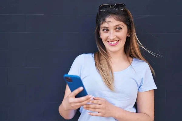 若いヒスパニック系の女性は黒の背景にスマートフォンを使用して自信を笑顔 — ストック写真