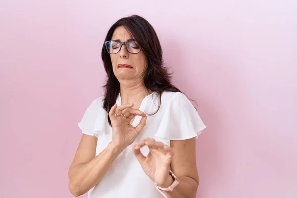 Middle age hispanic woman wearing casual white t shirt and glasses disgusted expression, displeased and fearful doing disgust face because aversion reaction.
