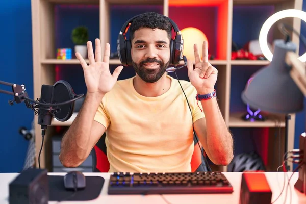自信と幸せ笑みを浮かべている間ヘッドフォンでビデオゲームをプレイし 指の数8を指しているヒスパニックな男 — ストック写真