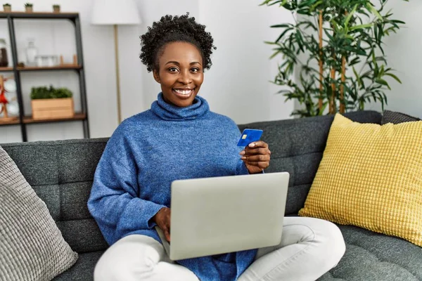 非洲裔美国妇女坐在家里沙发上 使用笔记本电脑和信用卡 — 图库照片