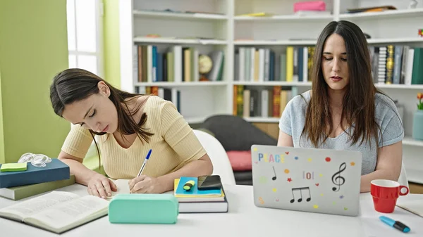 图书馆大学有两名妇女坐在桌面上学习使用笔记本电脑书写笔记 — 图库照片