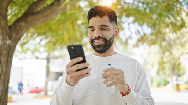 Jovem Hispânico Homem Segurando Garrafa Água Usando Smartphone Parque — Fotografia de Stock