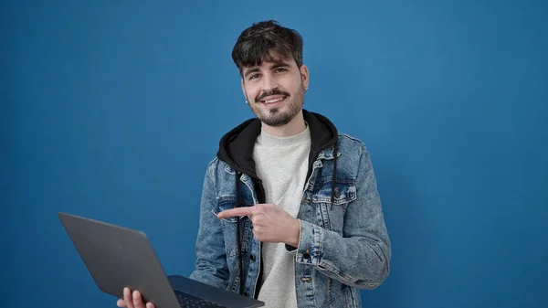 年轻的惊慌失措的男人笑着指着笔记本电脑 露出孤立的蓝色背景 — 图库照片