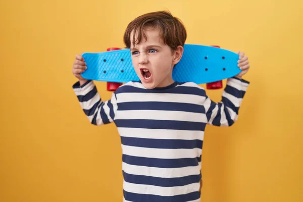 黄色を背景にスケートを保持する小さな白人の少年怒りと怒りの叫び不満と激怒し 怒りで叫んで怒っている 怒りと攻撃的な考え方 — ストック写真