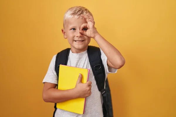 小さなCaucasian男の子身に着けている学生のバックパックと開催本笑顔幸せな行いますOk Signとともに手で目を通して見て指 — ストック写真