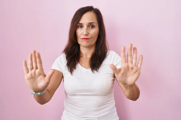 ピンクの背景の上に立つ中年のブルネットの女性は 恐怖と嫌な表情で拒否と否定を示す手の手のひらを離れて移動します 止めて禁止する — ストック写真
