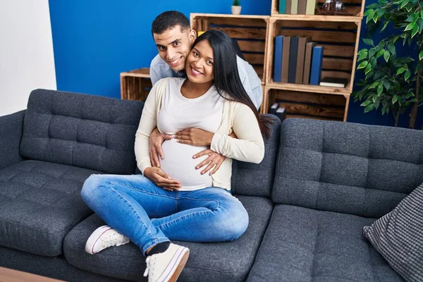 Young Latin Couple Expecting Baby Hugging Each Other Sitting Sofa — Zdjęcie stockowe