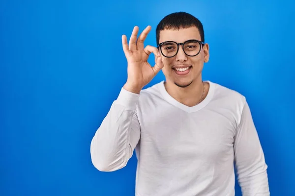 年轻的阿拉伯男子穿着随意的白色衬衫 戴着眼镜 面带微笑 手指手画脚地签了名 成功表达 — 图库照片