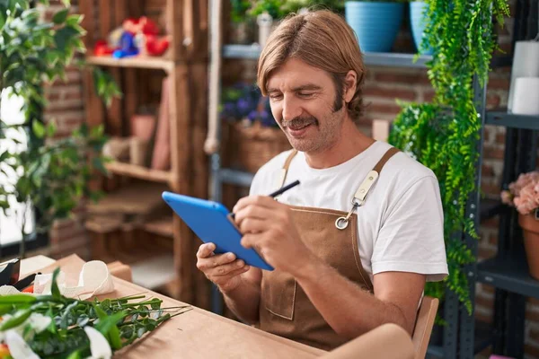 Young blond man florist smiling confident using touchpad at flower shop