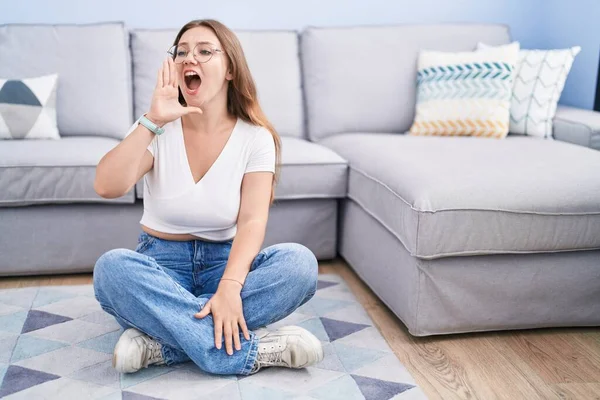 リビングルームの床に座って大声で叫び 口の上に手で横に大声で叫ぶ若い白人女性 コミュニケーションの概念 — ストック写真