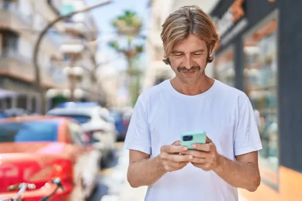 年轻的金发男人在街上用智能手机充满自信地微笑 — 图库照片