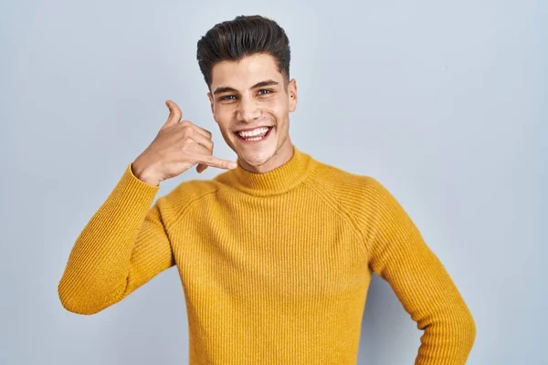 Jonge Spaanse Man Die Een Blauwe Achtergrond Staat Glimlachen Telefoongebaar — Stockfoto