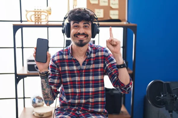 Junger Hispanischer Mann Mit Bart Zeigt Smartphone Bildschirm Musikstudio Lächelnd — Stockfoto