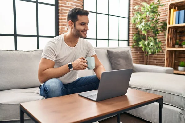 Young Hispanic Man Using Laptop Drinking Coffee Sitting Sofa Home —  Fotos de Stock