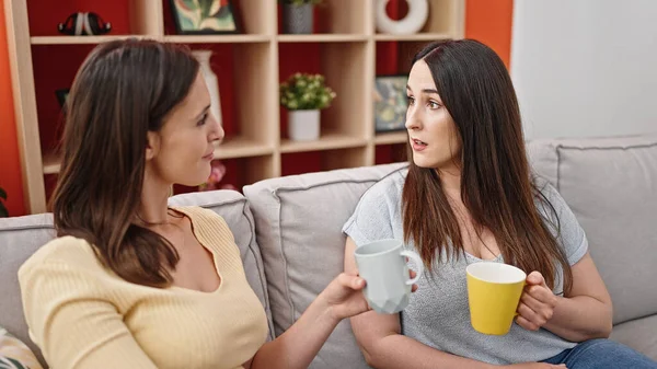 二人の女性がコーヒーを飲みながら家で話すソファに座って — ストック写真