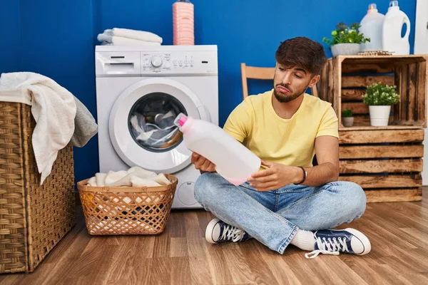 Young Arab Man Looking Detergent Bottle Sitting Floor Laundry Room — Stok fotoğraf