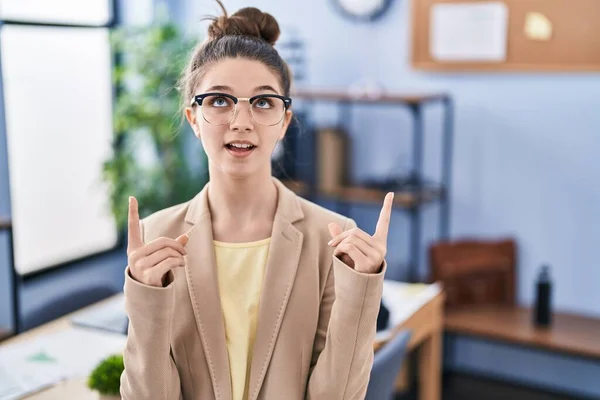 在办公室工作的少女戴着眼镜 惊讶地抬起头 用手指和胳膊指指点点着 — 图库照片