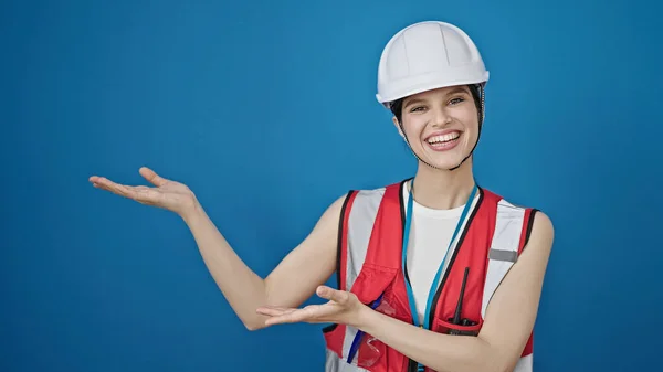 年轻美丽的惊慌失措的女建筑工人带着自信的笑容 呈现在孤独的蓝色背景上 — 图库照片