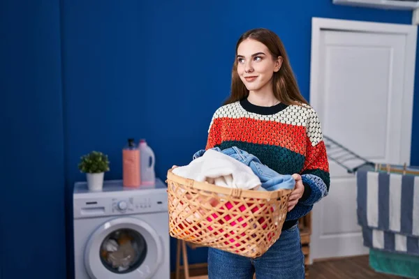 Çamaşır odasında çamaşır sepetini tutan kendine güvenen genç bir kadın.