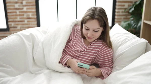 Młoda Blondynka Pomocą Smartfona Leżącego Łóżku Sypialni — Zdjęcie stockowe