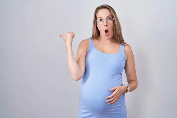若いです妊娠中の女性立ち上の白い背景驚きましたポインティングとともに手指へ側 口を開けて驚きの式 — ストック写真