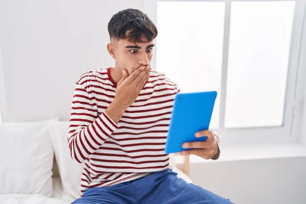 Jovem Hispânico Usando Touchpad Sentado Cama Cobrindo Boca Com Mão — Fotografia de Stock