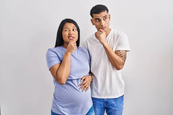 若いヒスパニック系のカップル期待している赤ちゃんの背景に立っている質問について心配し 心配し 顎に手で緊張 — ストック写真