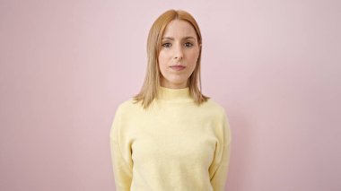 İzole edilmiş pembe arka planda rahat yüzü olan genç sarışın kadın.