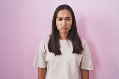 Young hispanic woman standing over pink background skeptic and nervous, frowning upset because of problem. negative person. 