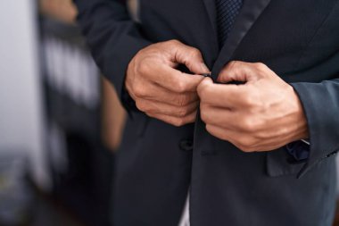 Genç kel iş adamı ofiste ceket giyiyor.