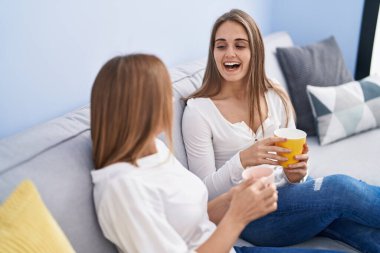 İki kadın anne ve kız evdeki kanepede oturup kahve içiyorlar.