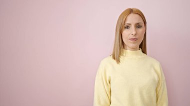 İzole edilmiş pembe arka planda rahat yüzü olan genç sarışın kadın.