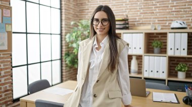 Genç, güzel, İspanyol bir iş kadını ofiste kendinden emin gülümsüyor.