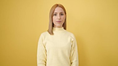 Young blonde woman standing with relaxed expression over isolated yellow background