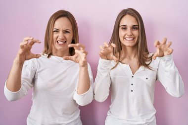 Orta yaşlı anne ve genç kız pembe arka planda durup komik bir şekilde gülüyorlar kedi gibi pençe hareketi yapıyorlar, agresif ve seksi bir ifade. 