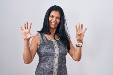 Beyaz arka planda duran olgun İspanyol kadın dokuz numarayı gösterip işaret ederken kendinden emin ve mutlu bir şekilde gülümsüyor.. 