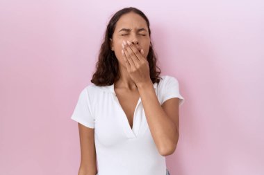 Günlük beyaz tişört giyen genç İspanyol kadın ağzını eliyle kapatmaktan sıkılmış. Huzursuz ve uykulu.. 