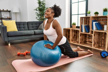 Afrika kökenli Amerikalı kadın evde formda top kullanarak karın kaslarını çalıştırıyor.