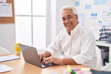 Ofiste çalışırken dizüstü bilgisayar kullanan orta yaşlı, kır saçlı bir iş adamı.