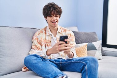 Evdeki kanepede oturan, akıllı telefon kullanan genç bir İspanyol.