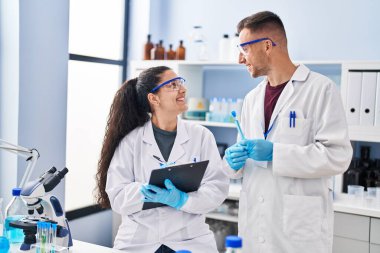 Man and woman wearing scientist uniform write on clipboard holding test tube at laboratory