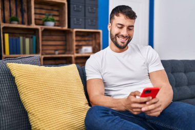 Evdeki kanepede oturan, akıllı telefon kullanan genç bir İspanyol.