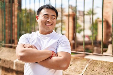 Young chinese man smiling confident standing with arms crossed gesture at street