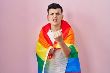 İkili olmayan kişi elinde gökkuşağı lgbtq bayrağı tutarken öfkeyle bağırıyor, öfkeyle bağırıyor ve el kaldırıyor. 