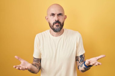 Sarı arka planda dikilen İspanyol dövmeli adam hiçbir şeyden habersiz ve kolları açık, hiçbir fikri yok.. 