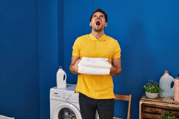 Mladý Hispánec Držící Čisté Ručníky Prádelně Vztekle Šíleně Křičící Frustrovaně — Stock fotografie