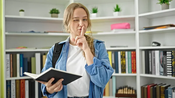 Young Blonde Woman Student Reading Book Doing Silence Gesture Library —  Fotos de Stock