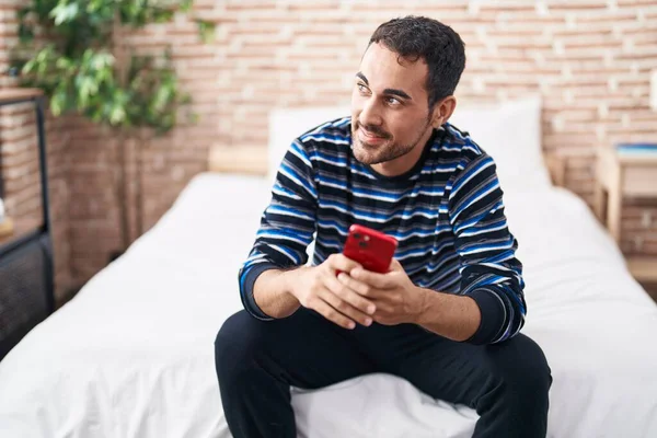 Junger Hispanischer Mann Sitzt Mit Smartphone Auf Bett Schlafzimmer — Stockfoto